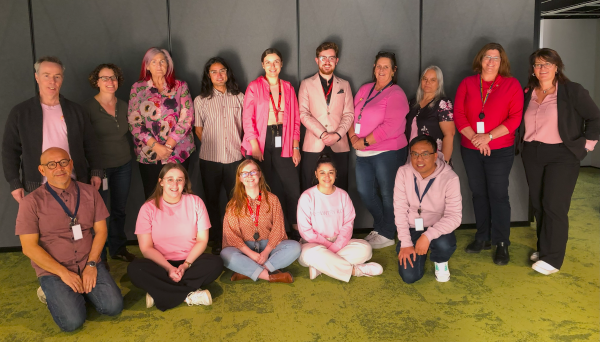 Group of people wearing pink shirts in front of a grey wall.