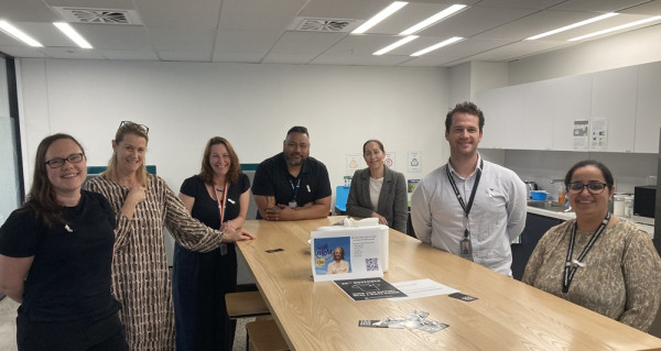 Group of Auckland staff members wearing white ribbons, gathered around a table with White Ribbon promotional material on it.